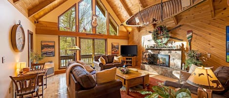 Large ADK style living room with stone fireplace, antler chandelier and canoe