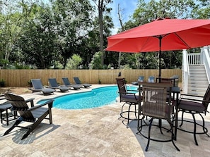 A private pool with lounge chairs for sunbathing, a dining table & chairs, and an umbrella.