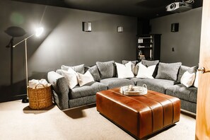 Relax and unwind in this cozy home theater, where plush seating and a projector create the perfect setup for movie nights. With ambient lighting and built-in shelves, it's an inviting space for ultimate comfort.