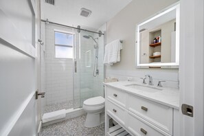 Bathroom with a walk-in glass shower, bright vanity lighting, and clean white finishes