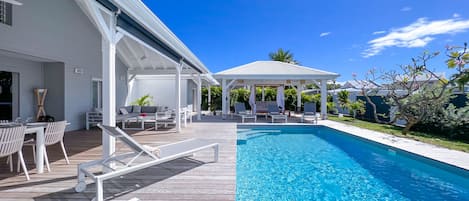 View of the swimming pool, wooden terrace, deckchairs and shaded patio with outdoor seating area