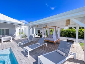 View of the patio with bed and sun loungers by the pool