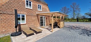 Terrasse mit Sitzmöbeln, Sonnenliegen, Sonnenschirm und Gasgrill