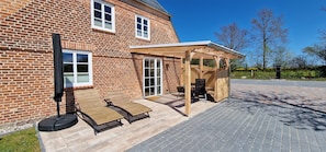 Terrasse mit Sitzmöbeln, Sonnenliegen, Sonnenschirm und Gasgrill