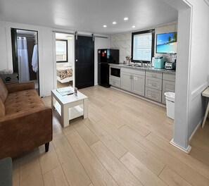 View of main room with leather sofa, kitchen, bathroom and private bedroom