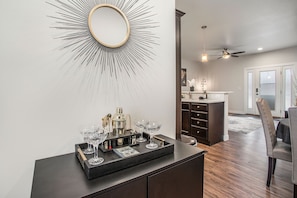 Elevate your cocktail experience with our luxury shaker set and elegant beverage glasses, complemented by a stylish gold mirror and views into the cozy living area.