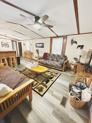 Relax in a spacious living area featuring two full-size futons, a ceiling fan, a large coffee table, and a Roku streaming TV. Conveniently adjacent to the kitchen for easy entertaining!