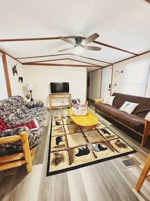Relax in a spacious living area featuring two full-size futons, a ceiling fan, a large coffee table, and a Roku streaming TV. Conveniently adjacent to the kitchen for easy entertaining!