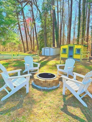 A fully fenced-in backyard featuring a kid-sized life playhouse, fire pit, soccer pool, corn hole boards, archery range, tetherball, and more!