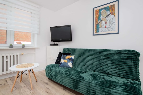 A corner of the living room with a green sofa, a mounted TV, and tasteful decor pieces.