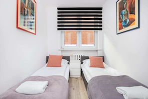 A bright bedroom with twin beds, soft bedding, and modern blinds, ideal for a comfortable stay.
