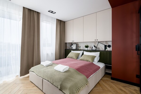 A stylish bedroom featuring a double bed with green and pink bedding, modern decor, and floor-to-ceiling windows with curtains.
