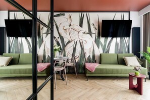 A cozy living area with a green sofa, floral wallpaper, and a well-lit ambiance.
