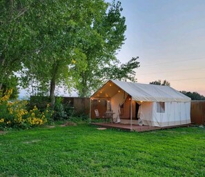 Tents are on a lush yard with gardens all around and a historic barn in view.