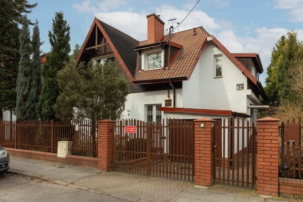 An exterior view of a charming house with a red brick facade and lush greenery surrounding it.
