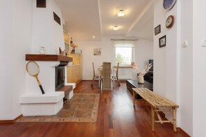 A cozy dining and living space with wooden floors, a fireplace, and warm lighting.
