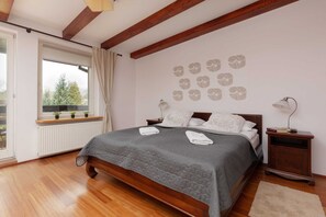 A bright bedroom with a wooden bed frame, exposed ceiling beams, and large windows.
