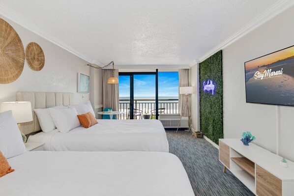 Bright, stylish oceanfront suite with two queen beds, a scenic balcony view, and modern decor. Features a lush accent wall with neon lighting, cozy seating area, and a large Smart TV. Perfect for a relaxing beach getaway!