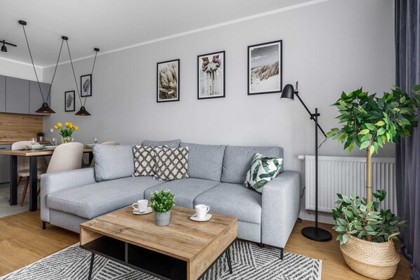 A stylish living room featuring a gray sofa, a patterned rug, and a small coffee table with a potted plant. Artwork decorates the wall, adding a modern touch.