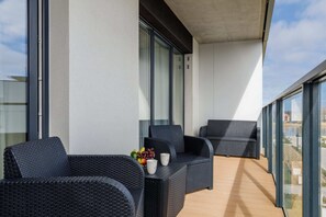 A balcony with a table and two chairs, offering a view of the surrounding area. The railing is modern, with a glass design.