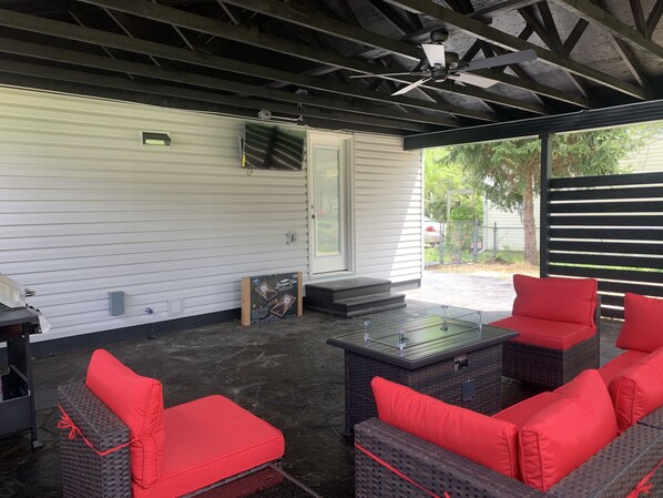 Comfortable patio furniture with a fire pit, a propane grill, 43” TV, & cornhole