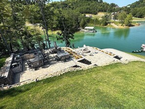 This view from the top porch looking down on the patios shows the large 16ft x 16 ft outdoor kitchen, lots of chairs to sit at the kitchen, 2 tables for eating, and an umbrella. You also see the 2nd patio with the firepit and the bottom patio for lounging.