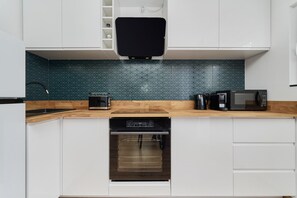 A modern kitchen featuring a turquoise tiled backsplash, white cabinets, and stainless steel appliances.

