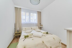 A bright bedroom with soft bedding, neutral decor, and large windows for natural light.
