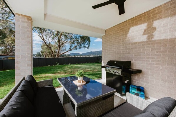  An undercover patio includes a BBQ and is comfortably furnished with a lounge setting for relaxed outdoor dining. 
