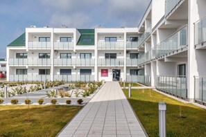 An exterior view of the apartment complex with modern architectural design. Green lawns and walking paths are visible, creating a welcoming atmosphere.