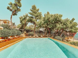 Amidst the green surroundings around the pool, towering trees create a natural canopy, enhancing the tranquil atmosphere of the space. Wooden benches and plush pillows create a secluded corner, inviting you to relax in the shade of nature's embrace, while the sea is just a few meters away, providing the perfect combination with the endless blue expanse of water.