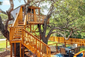 The treehouse is nestled between sprawling oak trees and overlooks the wooden decks and expansive sitting areas.