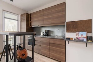 A modern kitchen with sleek wooden cabinets, white countertops, and a small window. Appliances like a microwave and induction stove are visible.