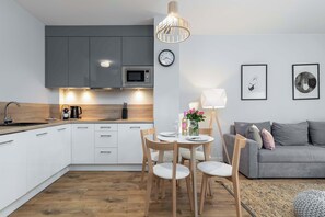 The round dining table with a white top coherently connects the cozy part of the living room with the functional kitchenette.