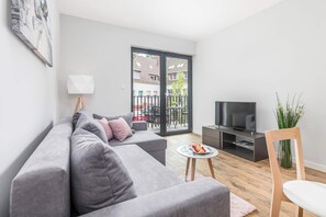 The bright living room with a fold-out grey sofa allows for relaxation and rest, while evening entertainment is provided by a flat-screen TV.