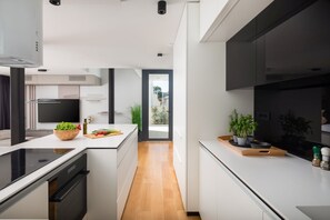 A view from the fully equipped kitchen with modern high tech appliances, a living room with a SMART LCD TV and doors to a side terrace with breakfast table with chairs