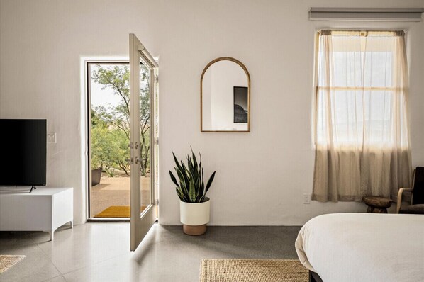 The bedroom area offers a luxurious King bed with natural-fiber linens, a sitting nook, and views of the desert mountains.