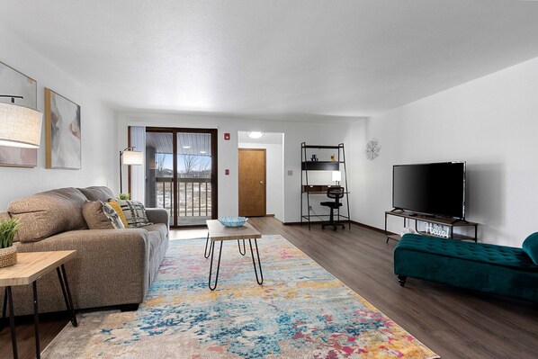 Bright + spacious living room. Features comfortable furnishings, smart tv, designated workspace, and balcony.