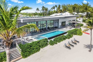 The pool deck features an infinity pool with spa, 2 dining cabanas, and walk-out access to a backyard beach.