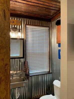 Industrial style bathroom with a reclaimed wood ceiling, and corrugated metal walls. 