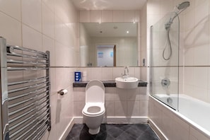 Fully tiled bathroom with a stylish washbasin vanity and huge mirror. Bathroom is well kept and stacked with essential toiletries. Bathroom has both bathtub and shower facility present.