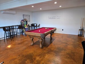 Game room in garage, foosball table, pool table, two arcade games, and TV.