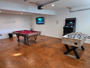 Game room in garage, foosball table, pool table, two arcade games, and TV.