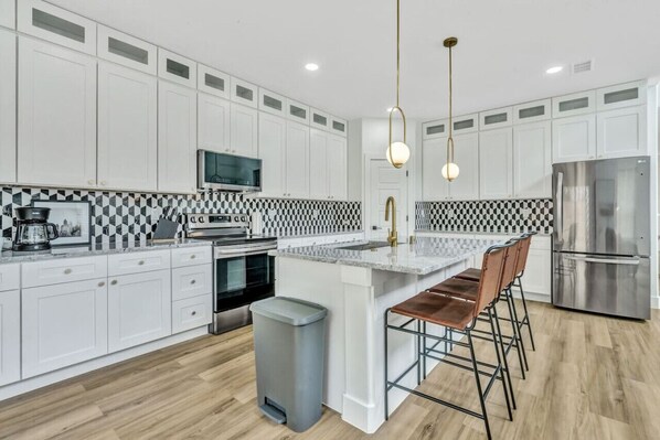 Prepare meals in this modern, fully-equipped kitchen featuring stainless steel appliances and a spacious island with bar seating. The open layout makes it easy to cook and entertain, ensuring a delightful culinary experience during your stay.