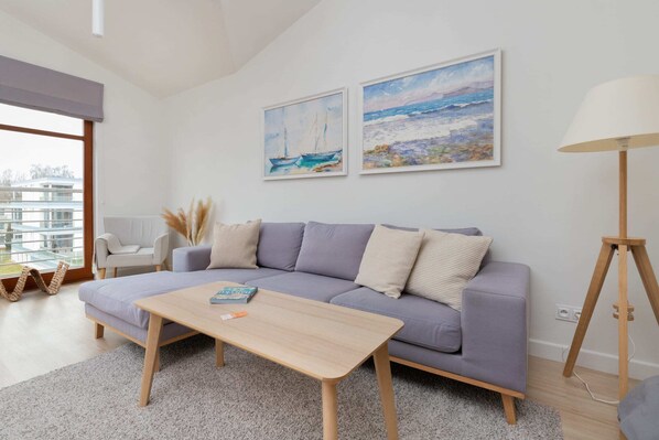 A bright living room featuring a comfortable sofa, light wooden furniture, and minimalist wall art.