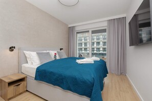 A stylish bedroom featuring a blue quilted bedspread, soft lighting, and large windows.
