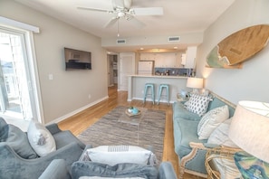 Vibrant coastal living room with teal sofa, jute rug, surfboard wall art, brand-new quartz countertops, and a stunning blue tile backsplash. A welcoming and serene space that perfect for a couples retreat or a family getaway. 