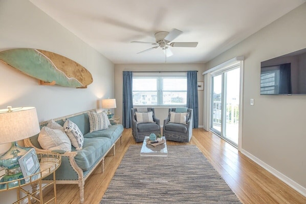 Step into this sunny coastal living room with surfboard art, light teal sofa, and natural textures, all illuminated by an abundance of natural light.