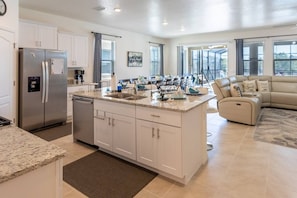 Kitchen, pantry and stove area along with plush living room with 75in smart OLED TV + dining area with seats for 12 at table and 4 at countertop.