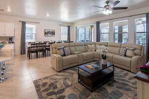 Plush living room with 75in smart OLED TV + dining area with seats for 12 at table and 4 at countertop.